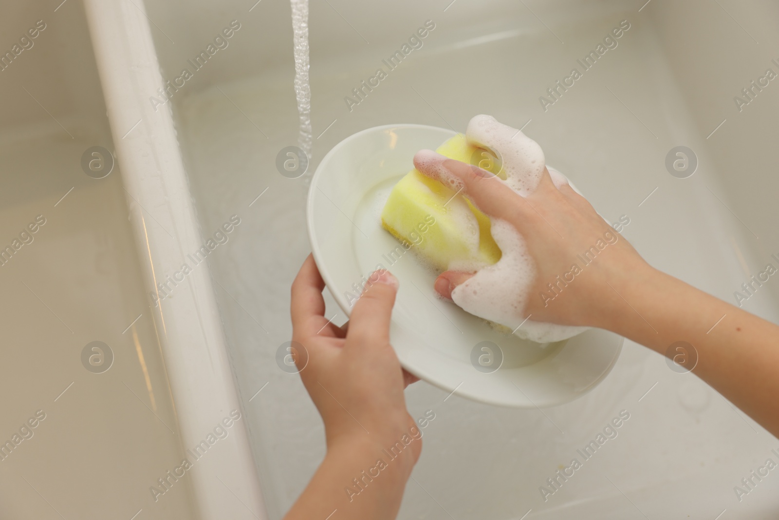 Photo of Little girl washing plate in sink, above view