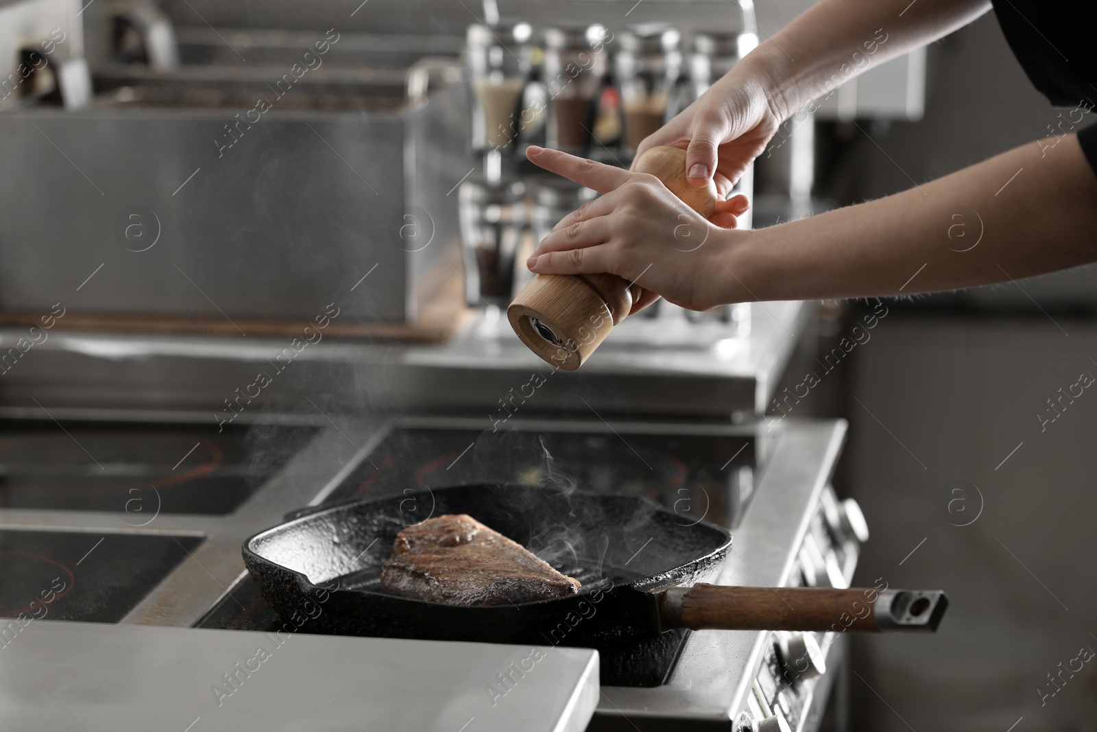 Photo of Female chef cooking meat on stove in restaurant kitchen, closeup