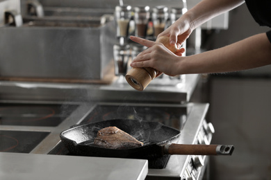 Female chef cooking meat on stove in restaurant kitchen, closeup