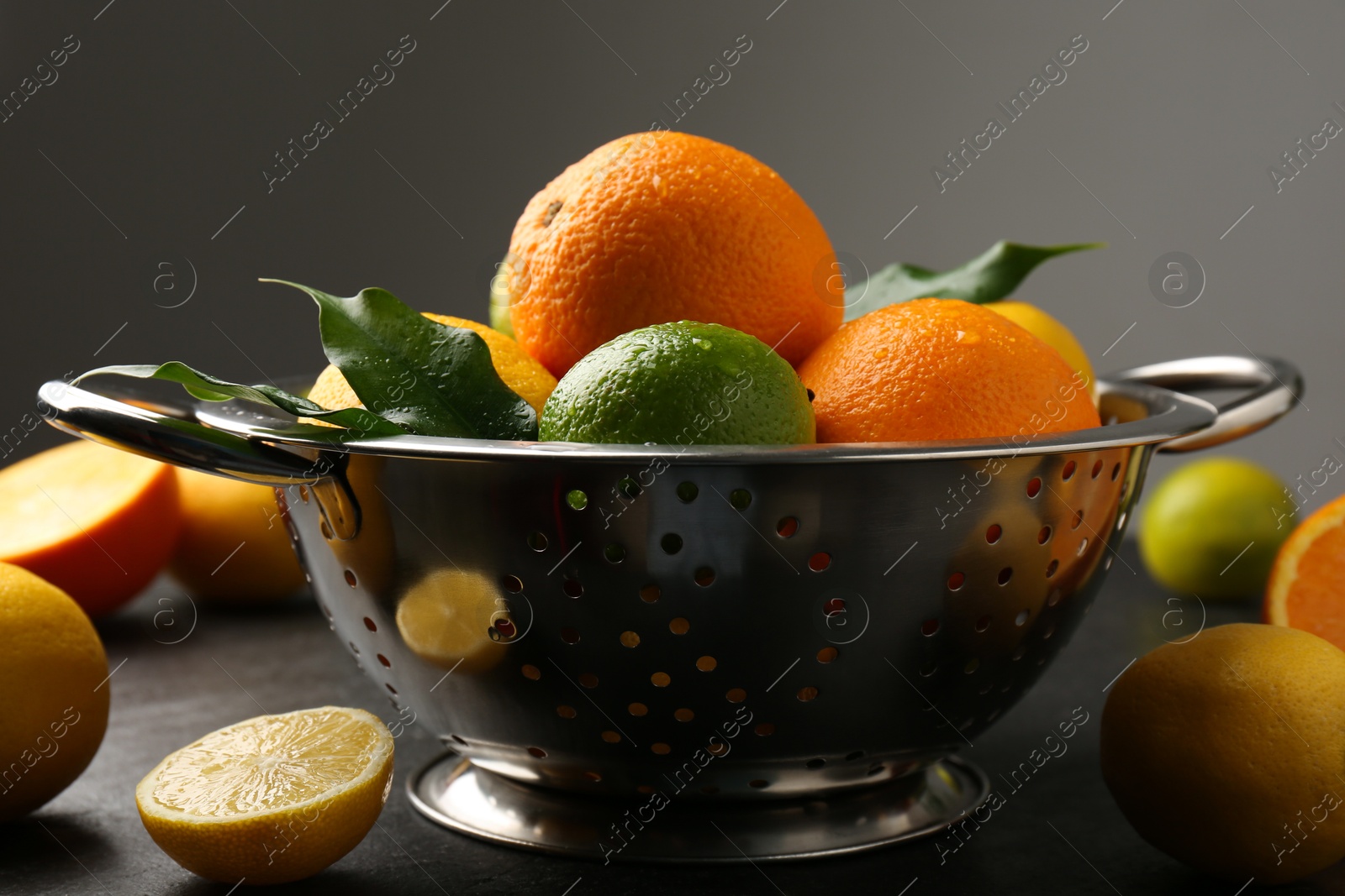 Photo of Fresh citrus fruits in colander on dark table, closeup