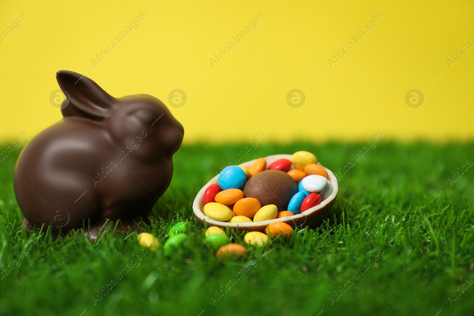 Photo of Chocolate Easter bunny, halved egg and candies on green grass