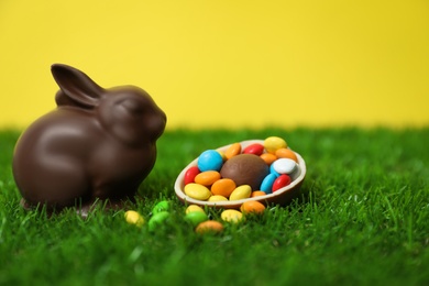 Chocolate Easter bunny, halved egg and candies on green grass