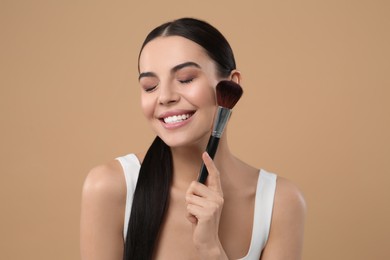 Photo of Beautiful woman with makeup brush on light brown background