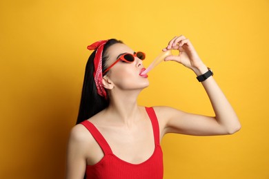 Photo of Fashionable young woman in pin up outfit chewing bubblegum on yellow background