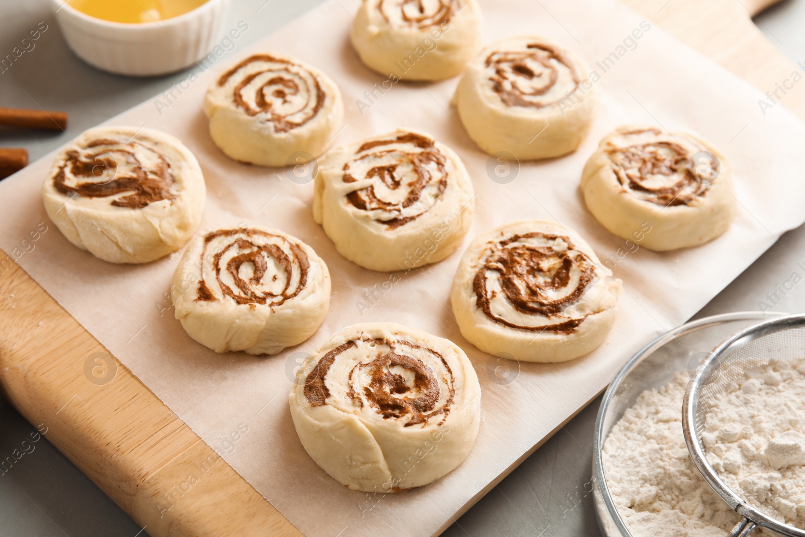 Photo of Wooden board with raw cinnamon rolls on table