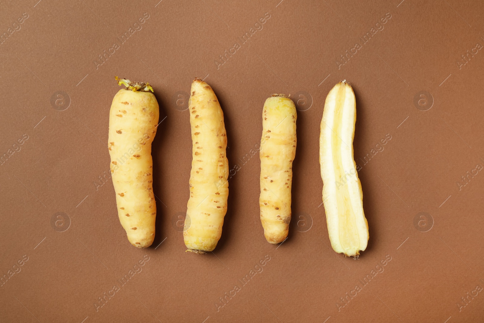 Photo of Whole and cut raw white carrots on brown background, flat lay