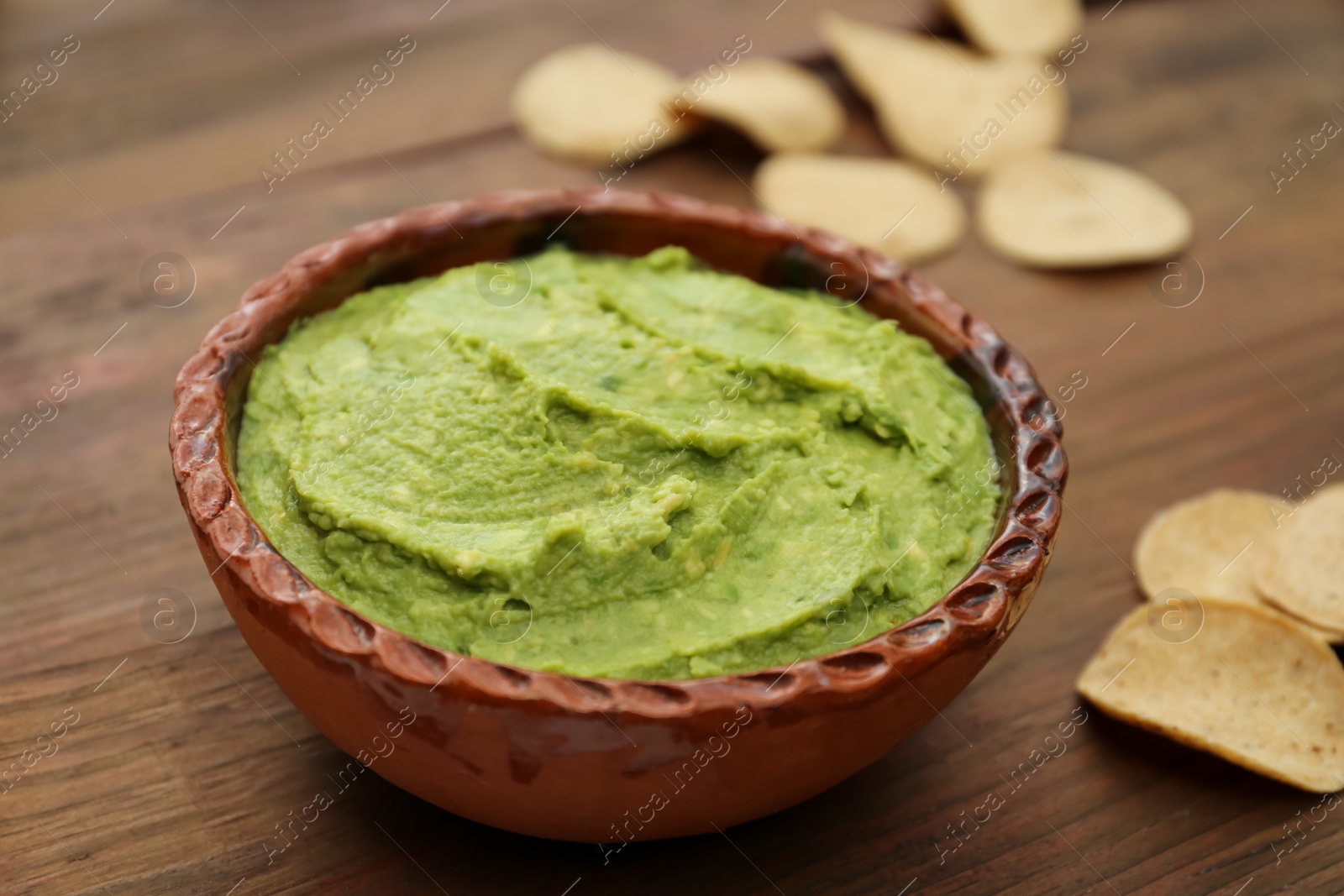 Photo of Delicious guacamole made of avocados and chips on wooden table, closeup