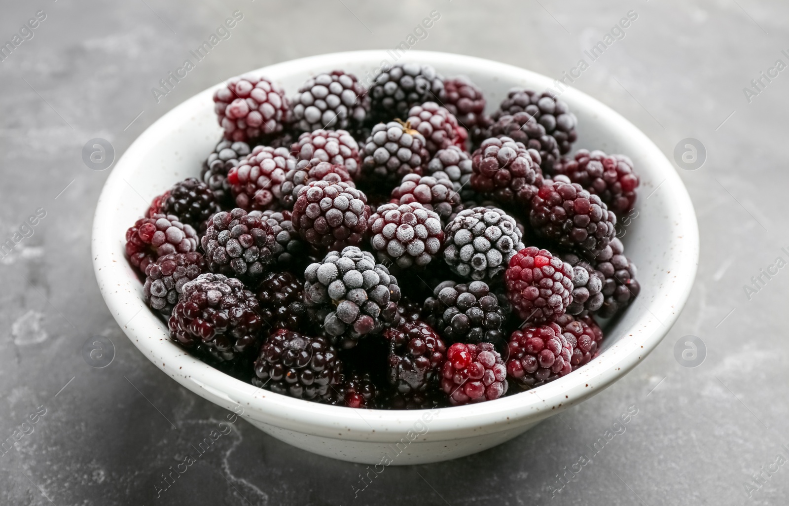 Photo of Tasty frozen blackberries in bowl on grey table, closeup