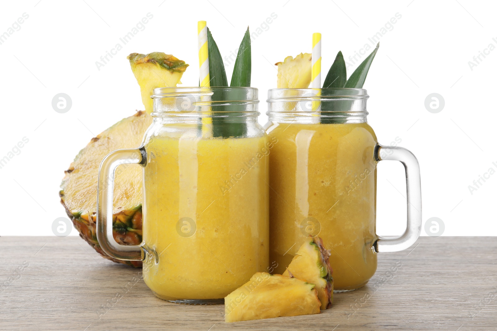 Photo of Tasty pineapple smoothie in mason jars and sliced fruit on wooden table against white background