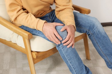 Photo of Man suffering from leg pain and touching knee on soft armchair indoors, closeup