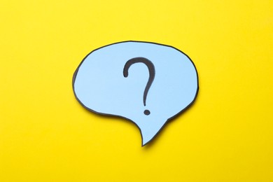 Photo of Paper speech bubble with question mark on yellow background, top view