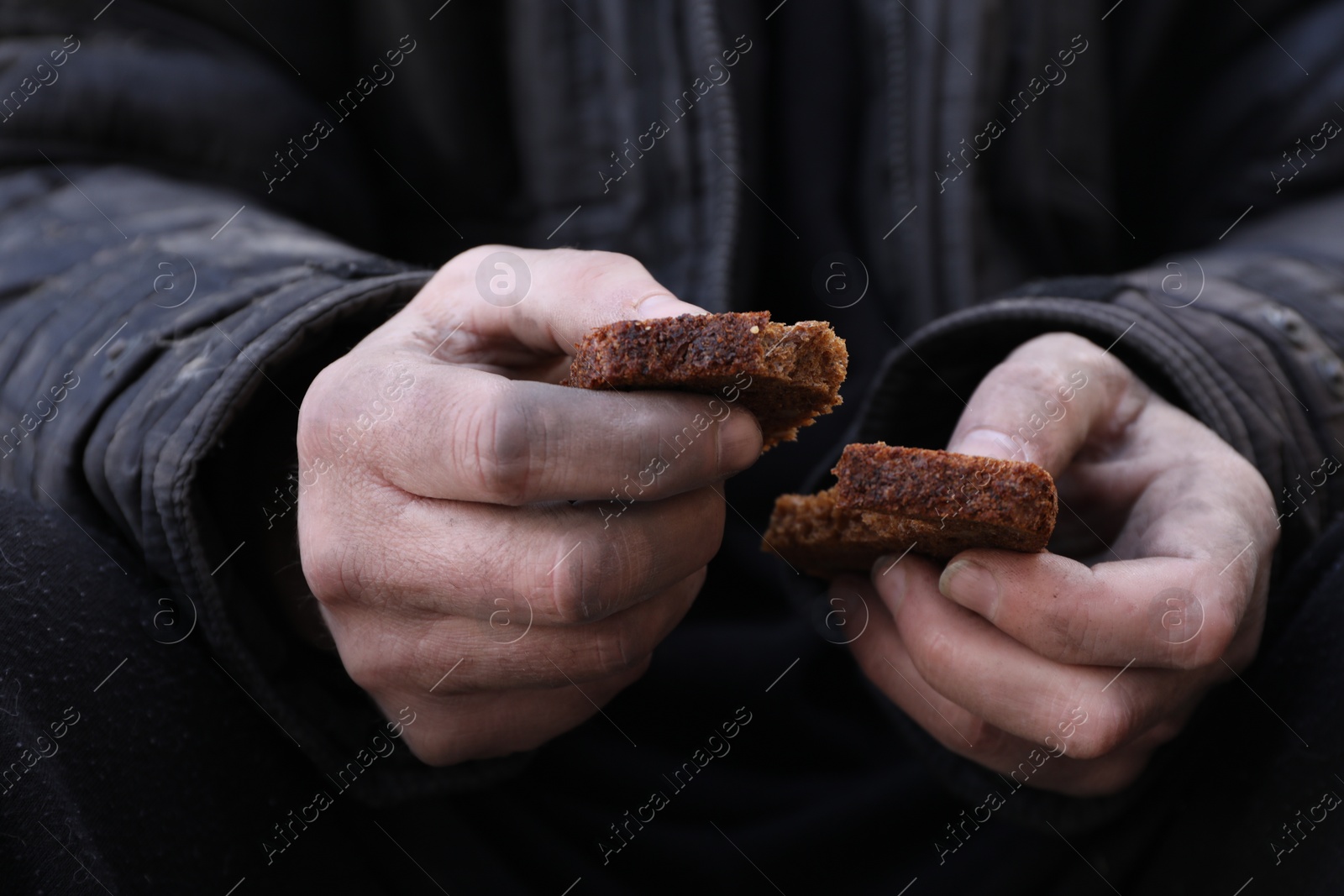 Photo of Poor homeless man holding piece of bread outdoors, closeup