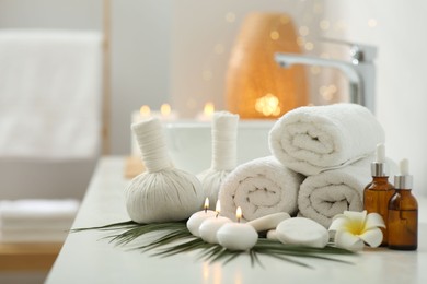 Photo of Spa composition. Rolled towels, herbal bags, cosmetic products and burning candles on white countertop in bathroom