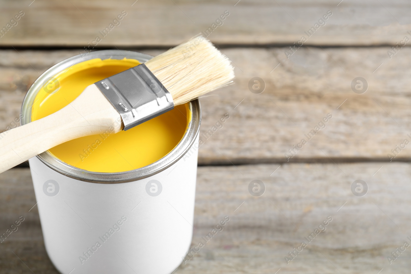 Photo of Can of yellow paint with brush on wooden table, closeup. Space for text