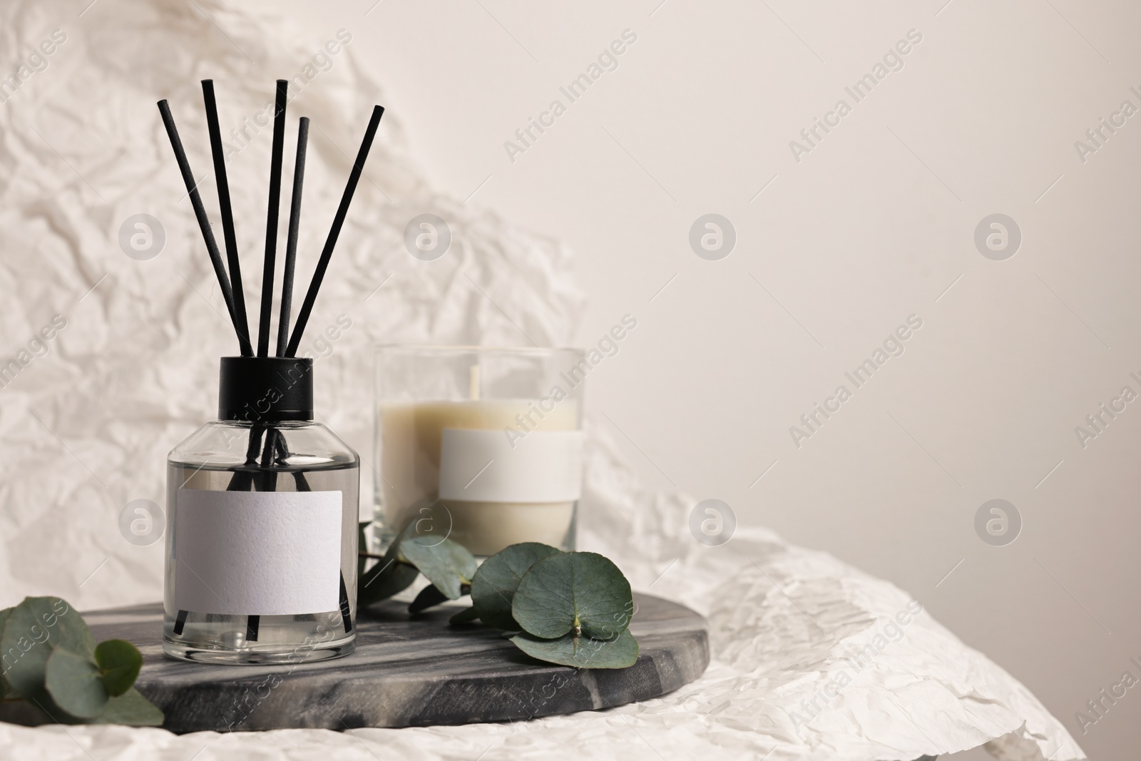 Photo of Aromatic reed air freshener, eucalyptus leaves and candle on white crumpled paper, space for text