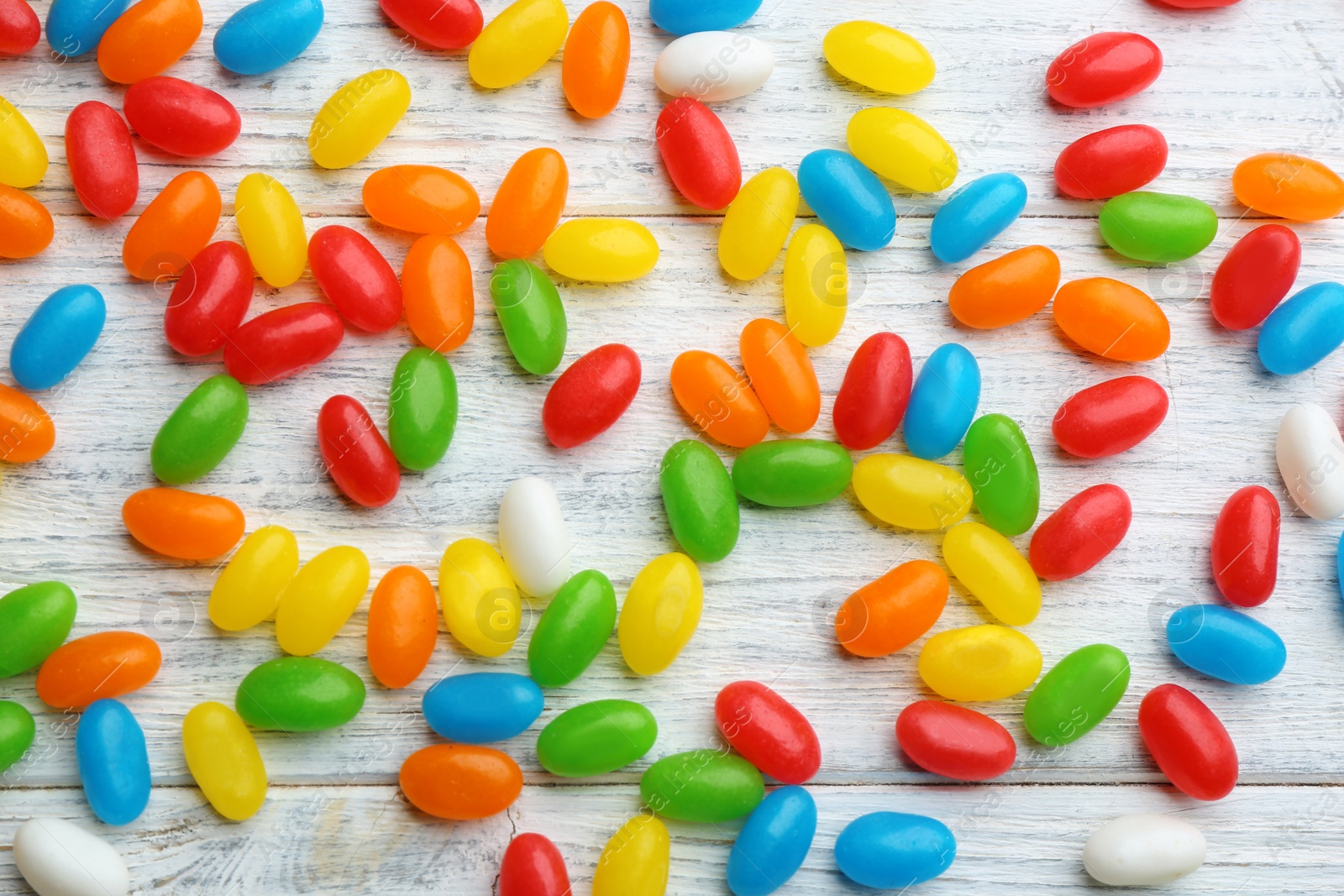 Photo of Colorful jelly beans on white wooden background, flat lay