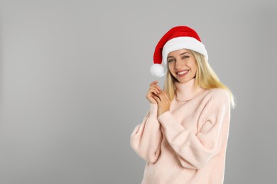 Photo of Happy woman in Santa hat on grey background, space for text. Christmas countdown