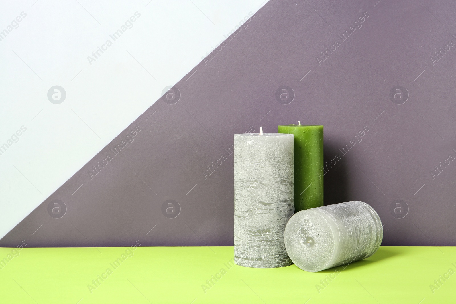 Photo of Decorative wax candles on table against color background