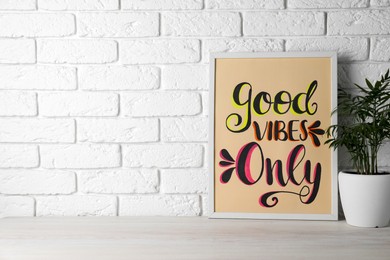 Photo of Board with phrase Good Vibes Only and houseplant on wooden table near white brick wall, space for text