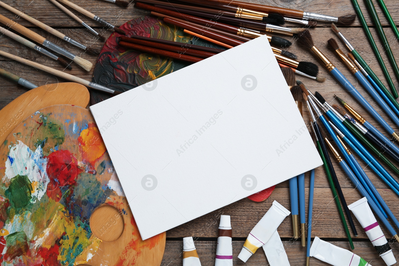 Photo of Blank canvas, brushes, palettes and paints on wooden table, flat lay. Space for text