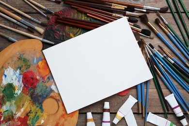 Photo of Blank canvas, brushes, palettes and paints on wooden table, flat lay. Space for text