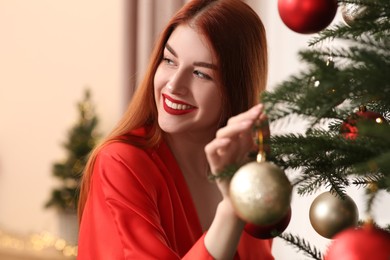 Beautiful young woman decorating Christmas tree at home