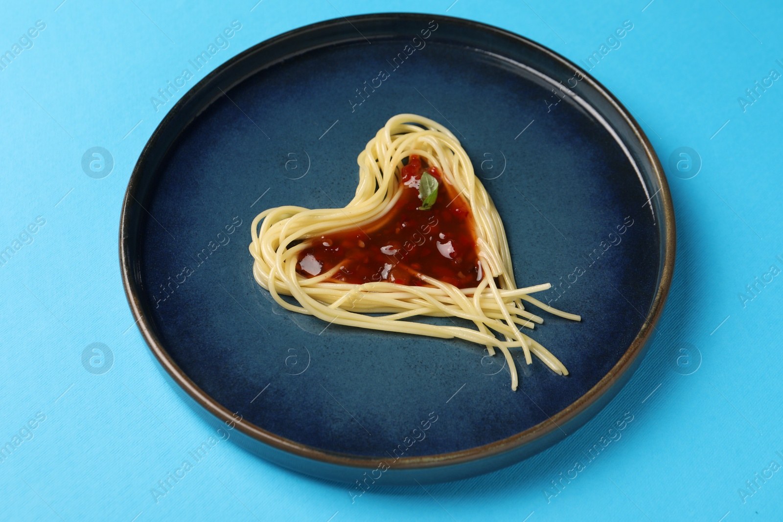 Photo of Heart made with spaghetti and sauce on light blue background