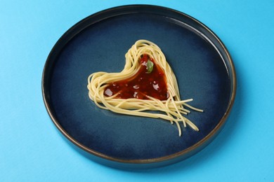 Photo of Heart made with spaghetti and sauce on light blue background