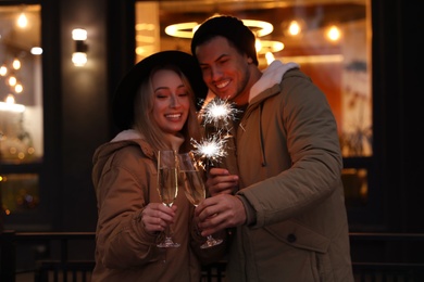 Photo of Happy couple with sparklers and glasses of champagne at winter fair
