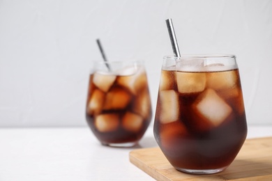 Photo of Glass of tasty cola with ice cubes on white table, closeup. Space for text