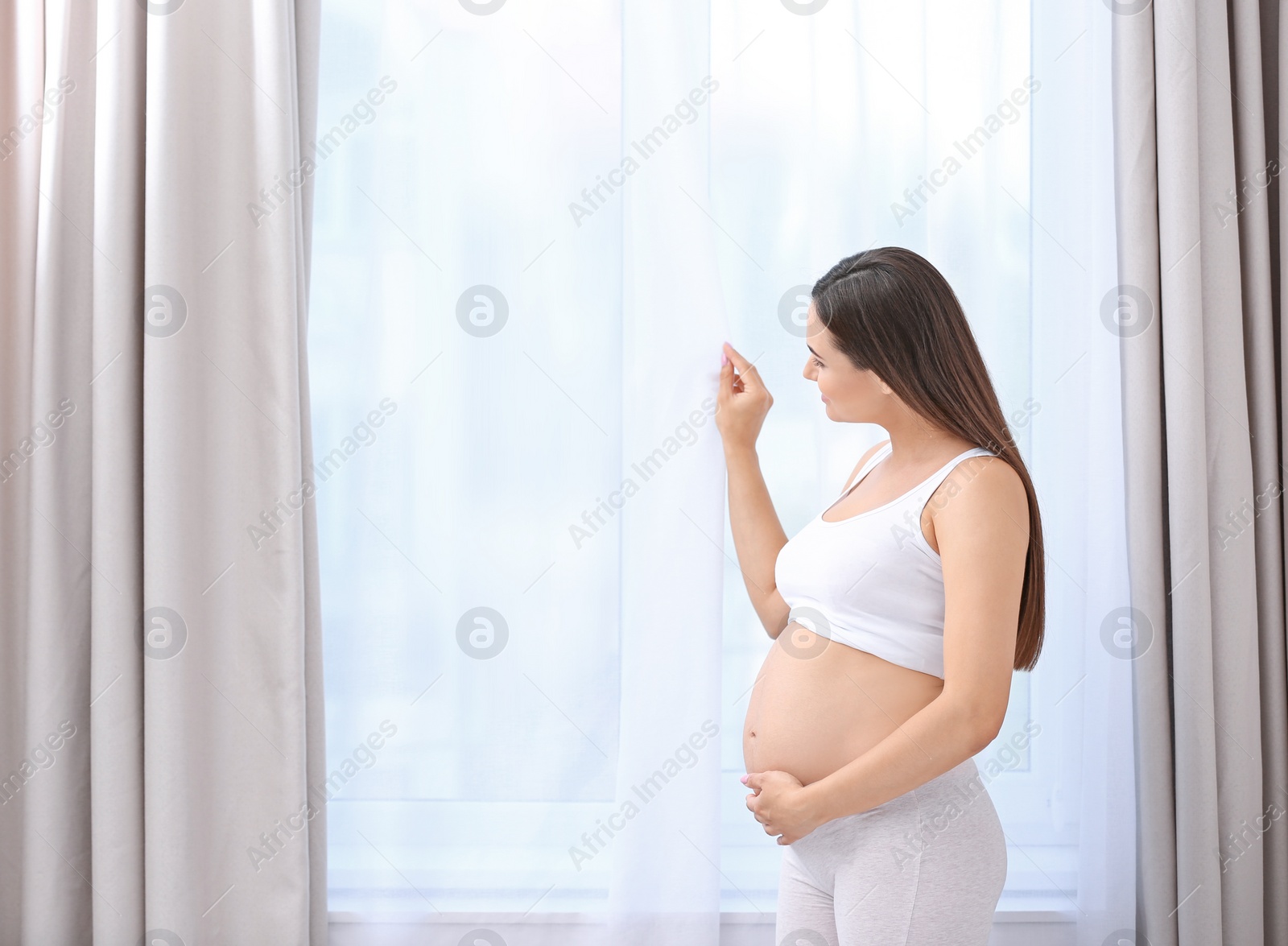 Photo of Young beautiful pregnant woman near window at home