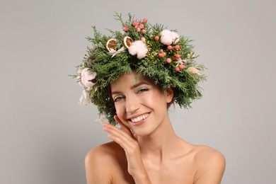 Happy young woman wearing wreath on grey background