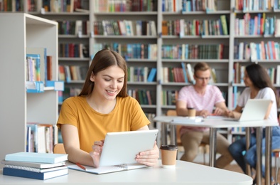 Young woman working on tablet at table in library. Space for text