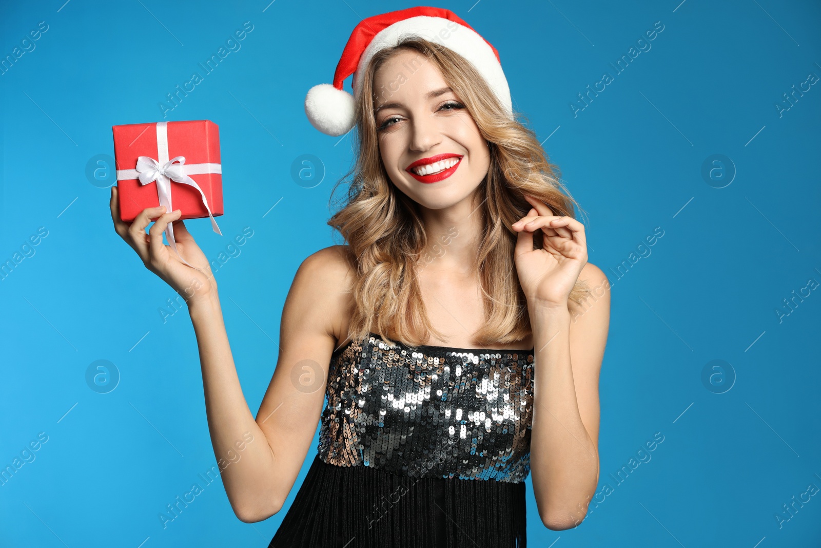 Photo of Happy young woman wearing Santa hat with Christmas gift on light blue background