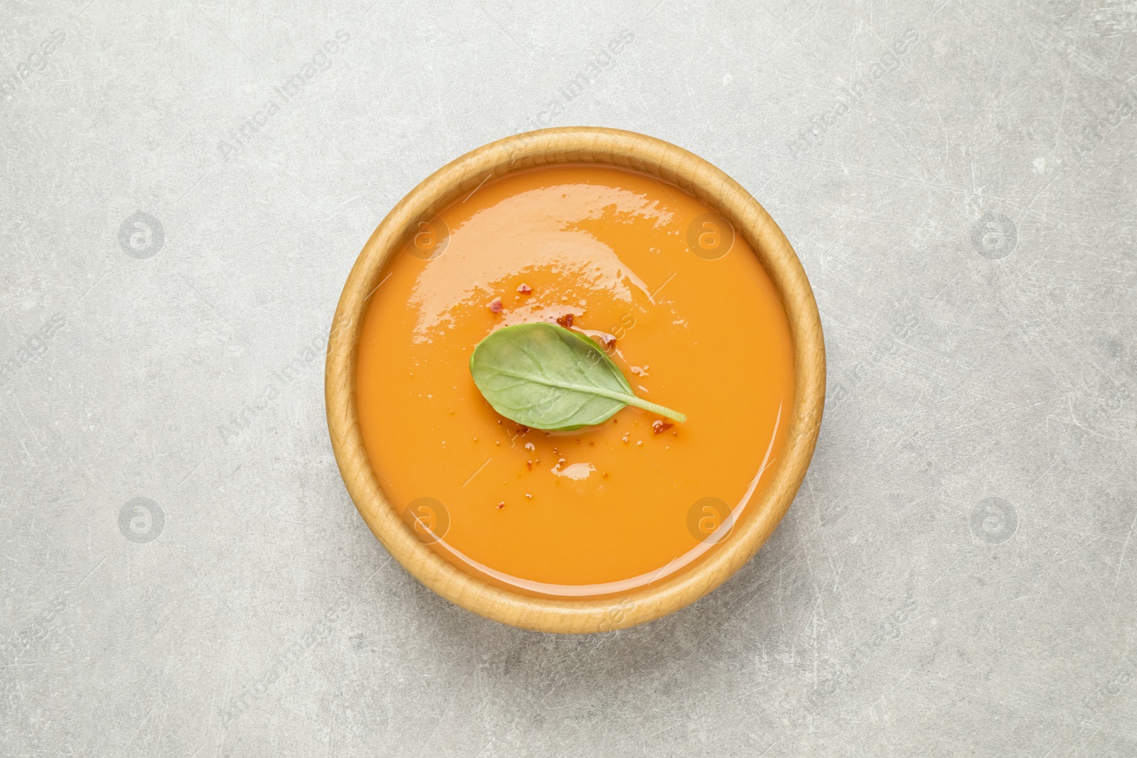 Photo of Tasty creamy pumpkin soup with basil in bowl on light grey table, top view