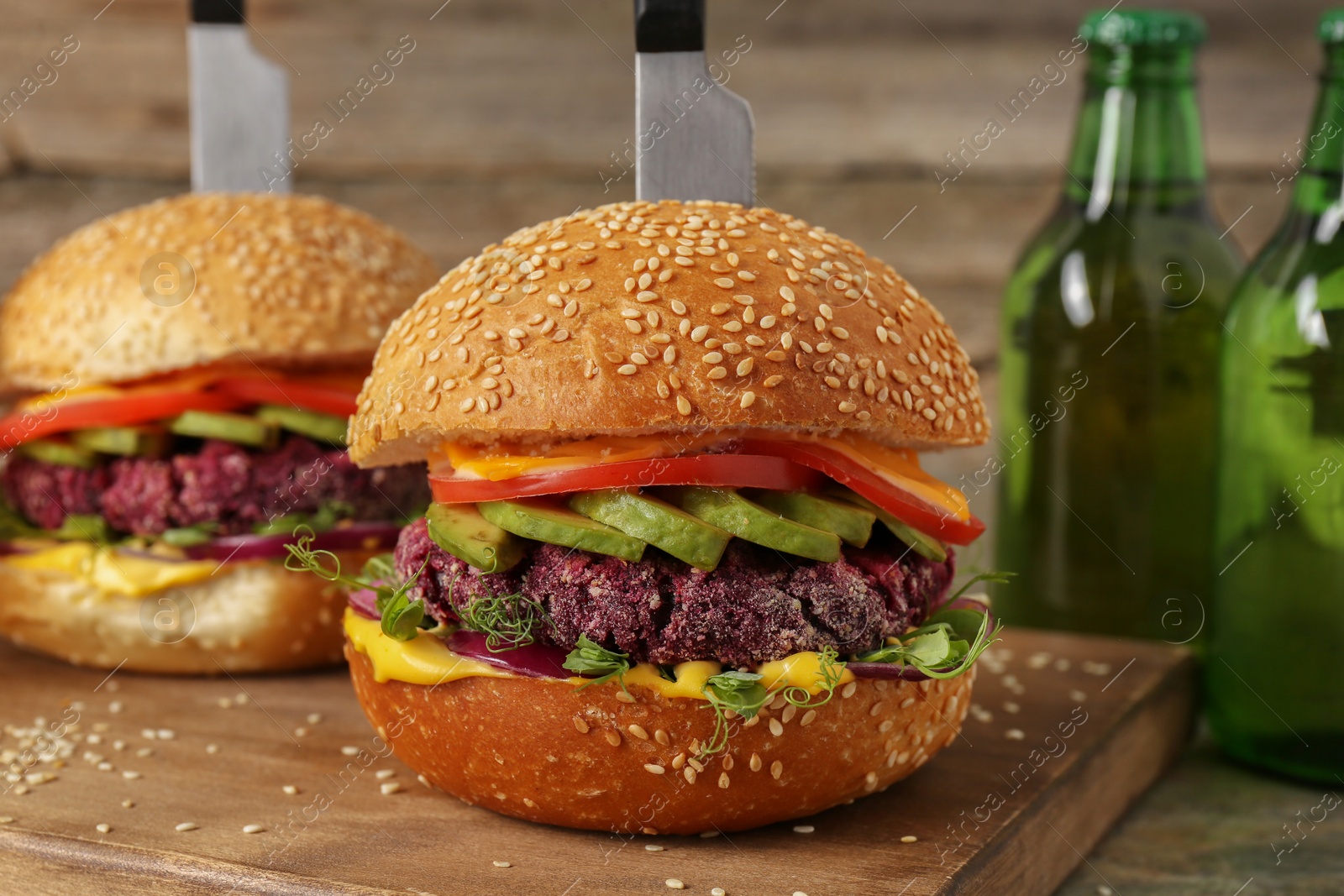 Photo of Tasty vegetarian burgers with beet cutlets, cheese, avocado and tomatoes served on wooden table, closeup