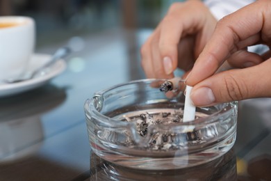 Photo of Women putting out cigarettes in ashtray at table, closeup