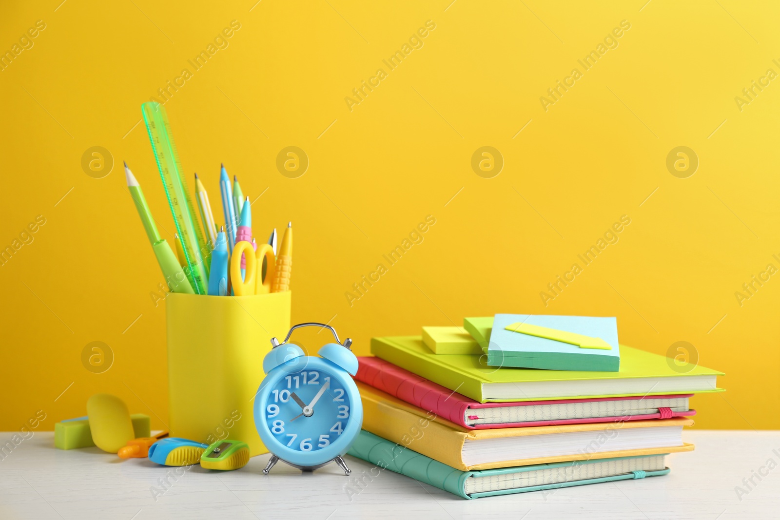 Photo of Different school stationery on white wooden table against yellow background