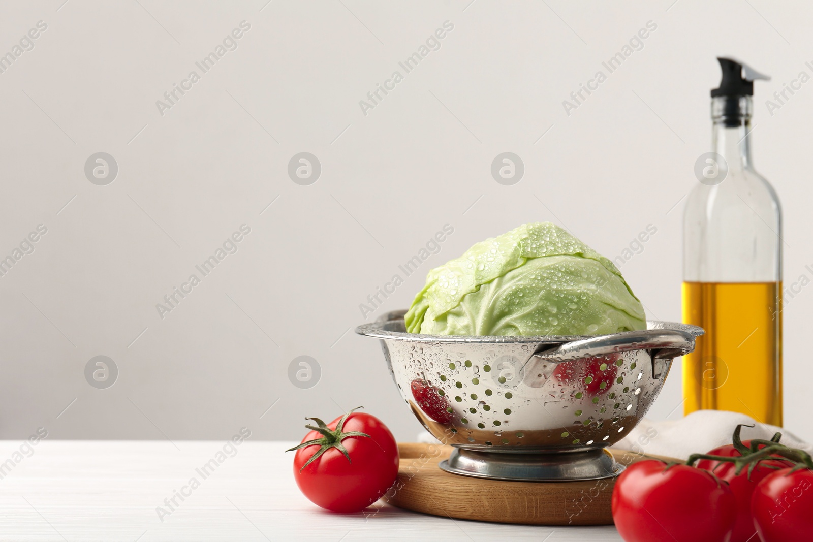 Photo of Wet cabbage in colander and tomatoes on white wooden table, closeup. Space for text