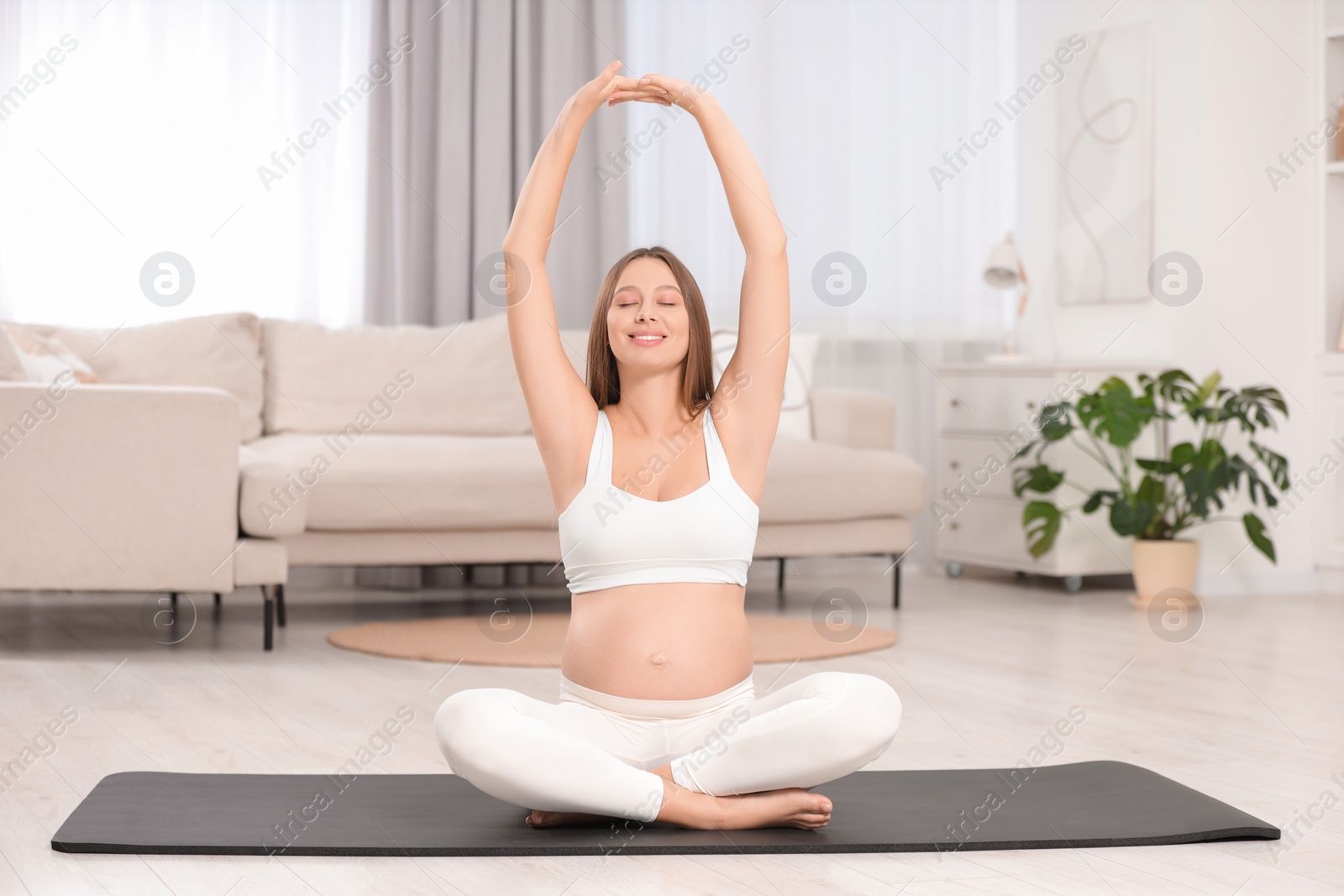 Photo of Pregnant woman stretching on yoga mat at home