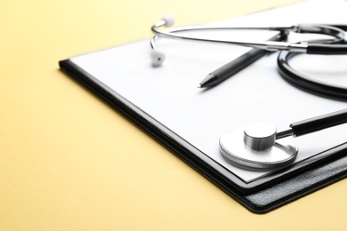 Clipboard with stethoscope and pen on yellow background, closeup. Space for text