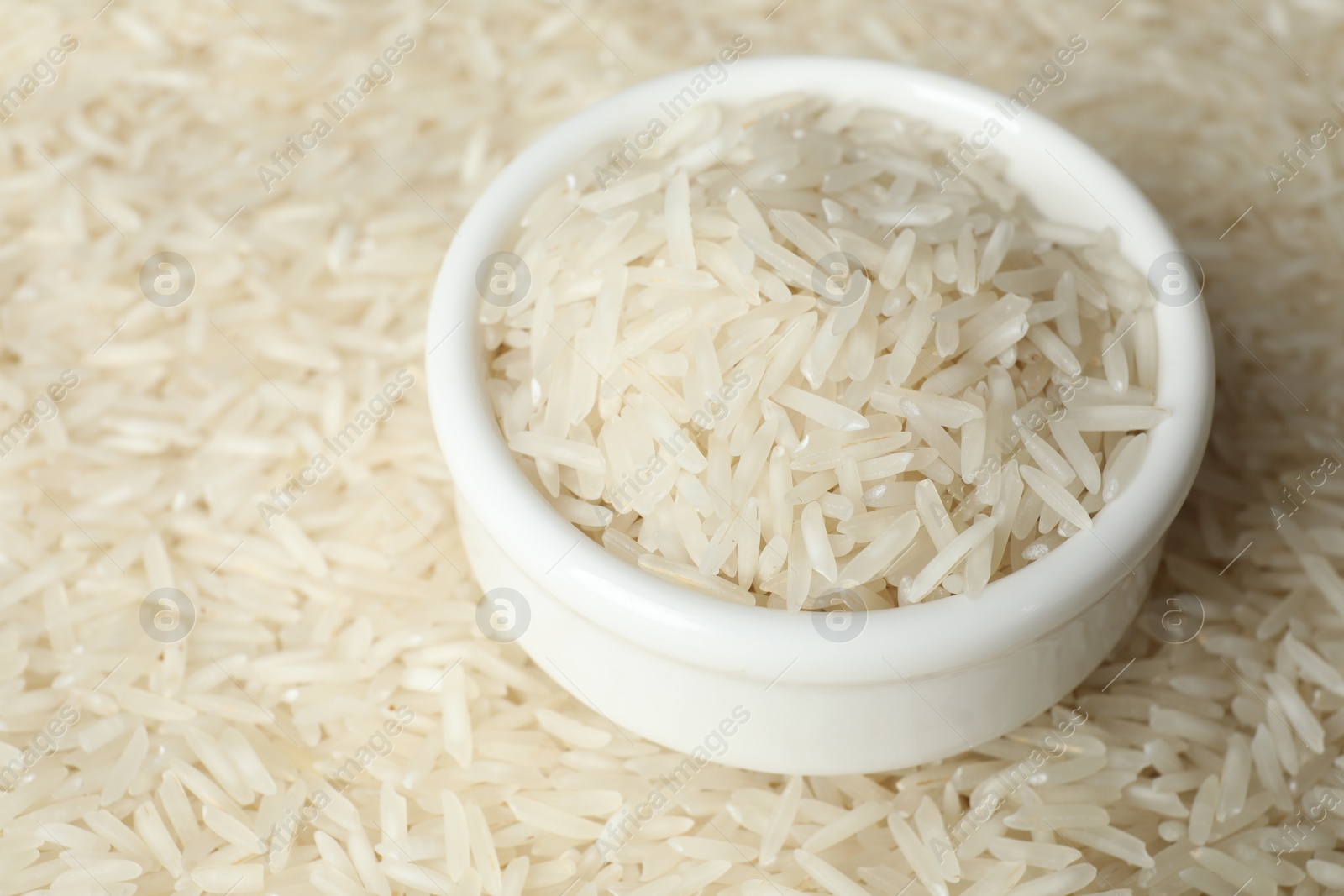 Photo of Raw basmati rice and bowl as background, closeup. Space for text