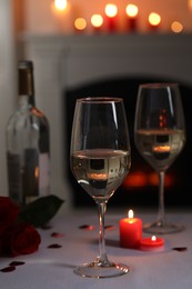 Glasses of white wine, rose flowers and burning candles on grey table indoors. Romantic atmosphere