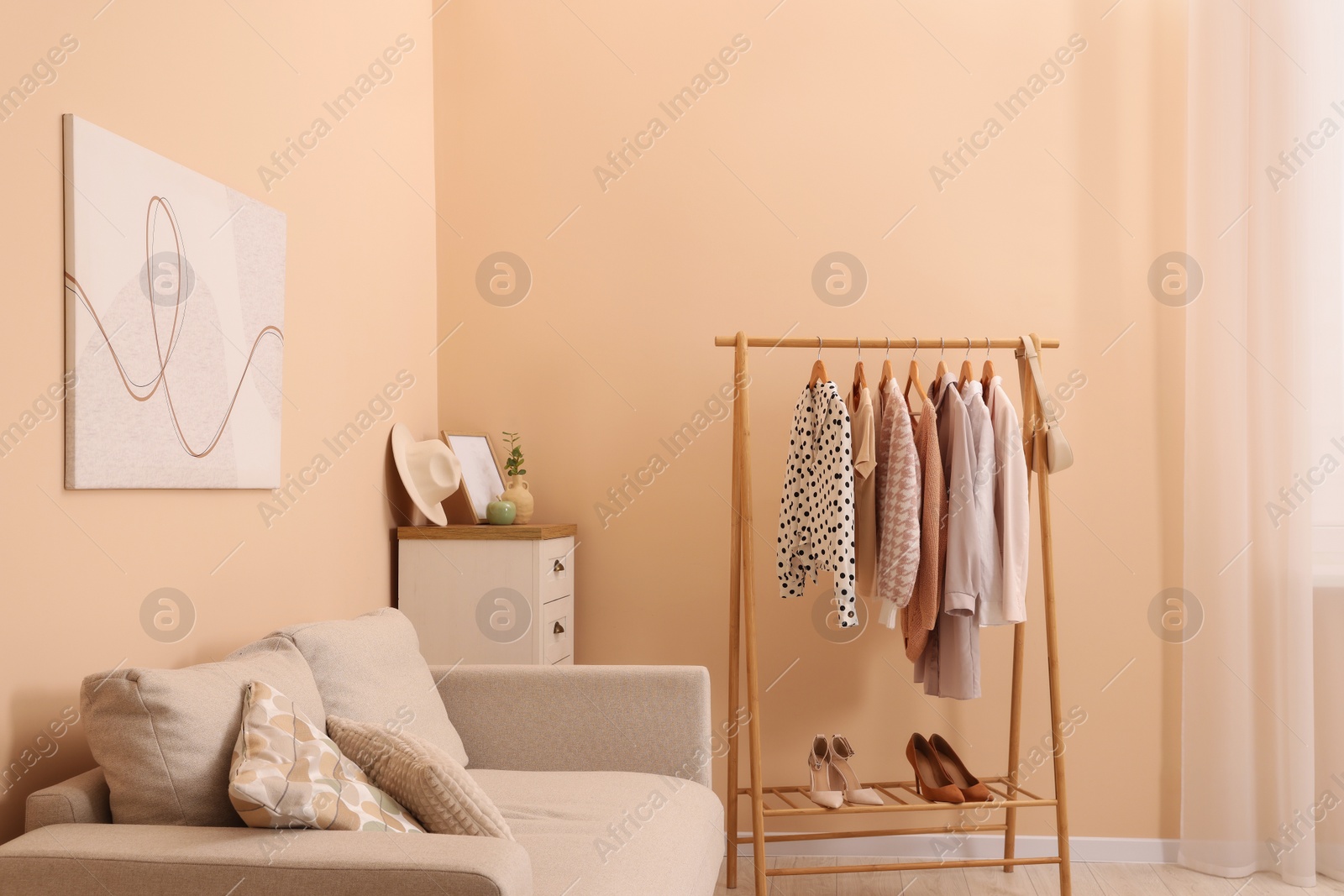 Photo of Stylish living room interior with comfortable sofa and clothing rack