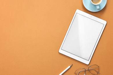 Modern tablet, glasses, stylus and cup of coffee on orange background, flat lay. Space for text