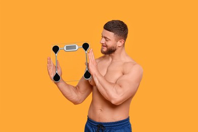 Photo of Athletic man holding scales on orange background. Weight loss concept