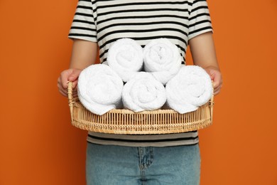 Photo of Woman holding wicker tray with rolled soft terry towels on orange background, closeup