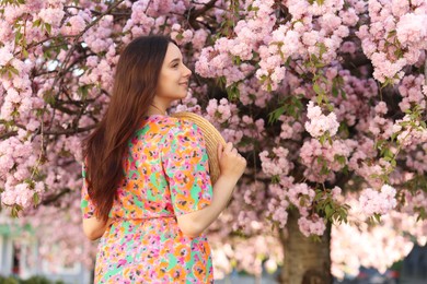 Beautiful woman with straw hat near blossoming tree on spring day