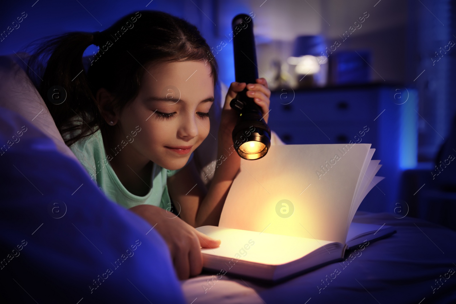 Photo of Little girl with flashlight reading fairy tale in dark bedroom