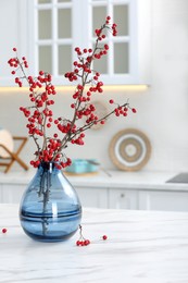 Photo of Hawthorn branches with red berries on table in kitchen